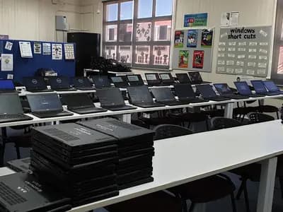Rows of laptops on desks in an empty school computer room