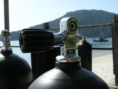 A technical diver descending through deep open water with multiple gas cylinders visible
