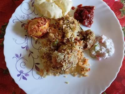 A plate of chicken biryani served with raita, a spoonful of pickle and a papad