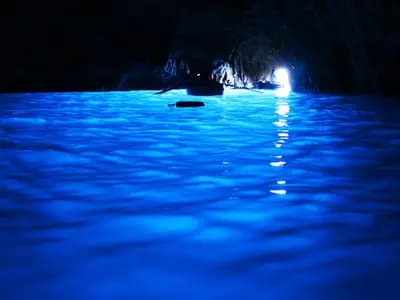 A technical diver silhouetted at the entrance of a deep underwater cave, lit by a dive torch
