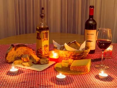 A rustic table with a bottle of olive oil, crusty bread, tomatoes and a bowl of mixed nuts