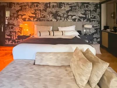 A rich, layered interior with chocolate brown walls, jewel-tone textiles, and mixed vintage and modern furnishings