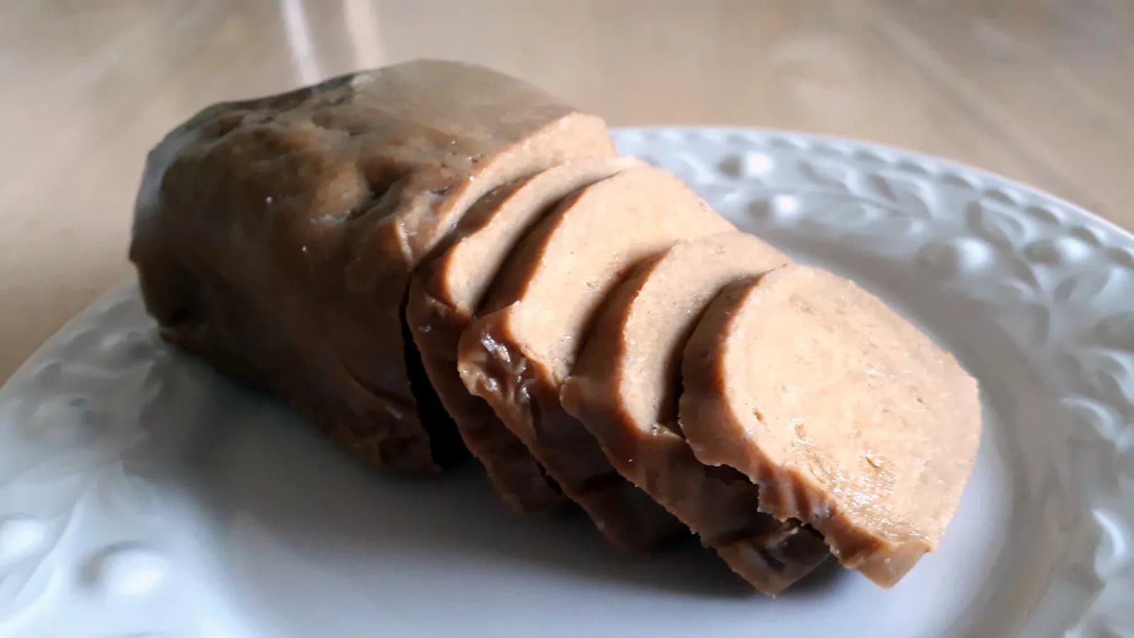 A poached seitan log part sliced on a plate, showing the dense fibrous interior that wheat gluten develops