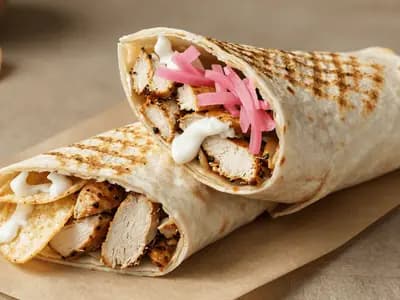 A tightly rolled chicken wrap cut in half, pickles and chips visible in the filling
