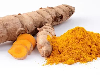 Fresh turmeric rhizome, sliced to show the orange interior, beside a heap of the ground spice. The concern in this piece is with concentrated capsules rather than with the spice itself