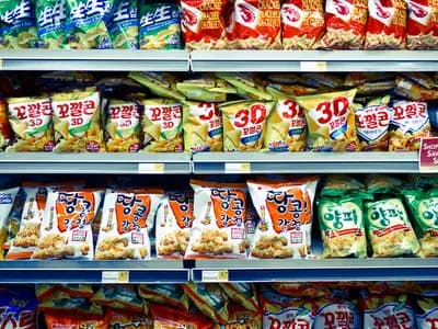 A supermarket aisle shelf stocked with brightly packaged snack products next to a produce section