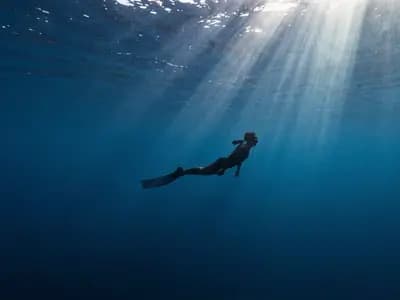 A freediver silhouetted in deep blue water under converging light rays