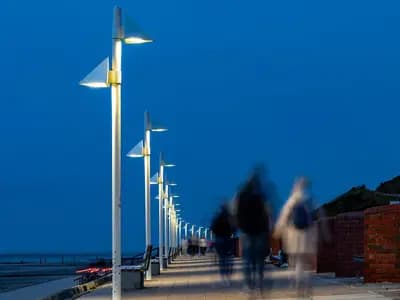 People walking along a lit seafront promenade at dusk, slightly blurred by the long exposure, with the beach to the left