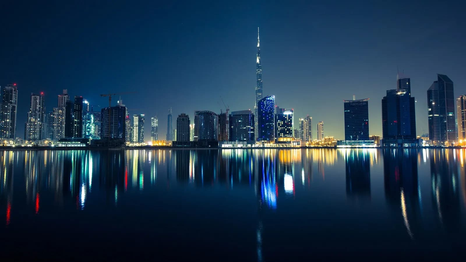 The Dubai skyline at night, with the Burj Khalifa at its centre and the towers of Business Bay reflected in the water