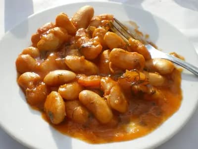 A plate of gigantes plaki, large white beans in a thick tomato and olive oil sauce, with a fork