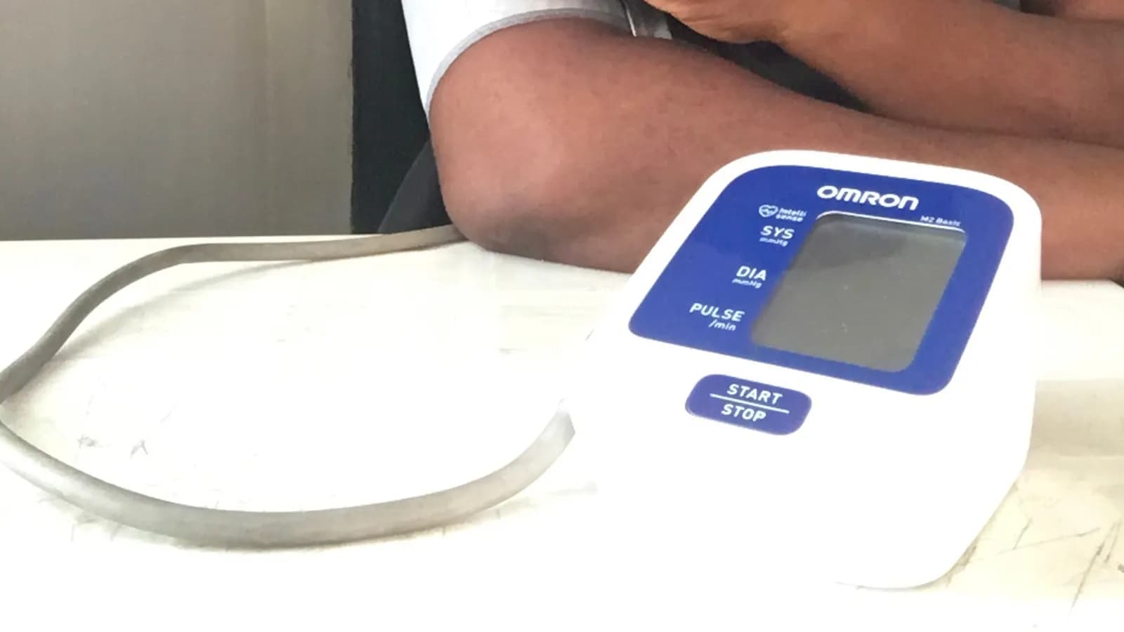 An automatic upper-arm home blood pressure monitor on a table beside a person's bare arm, photographed in April 2024