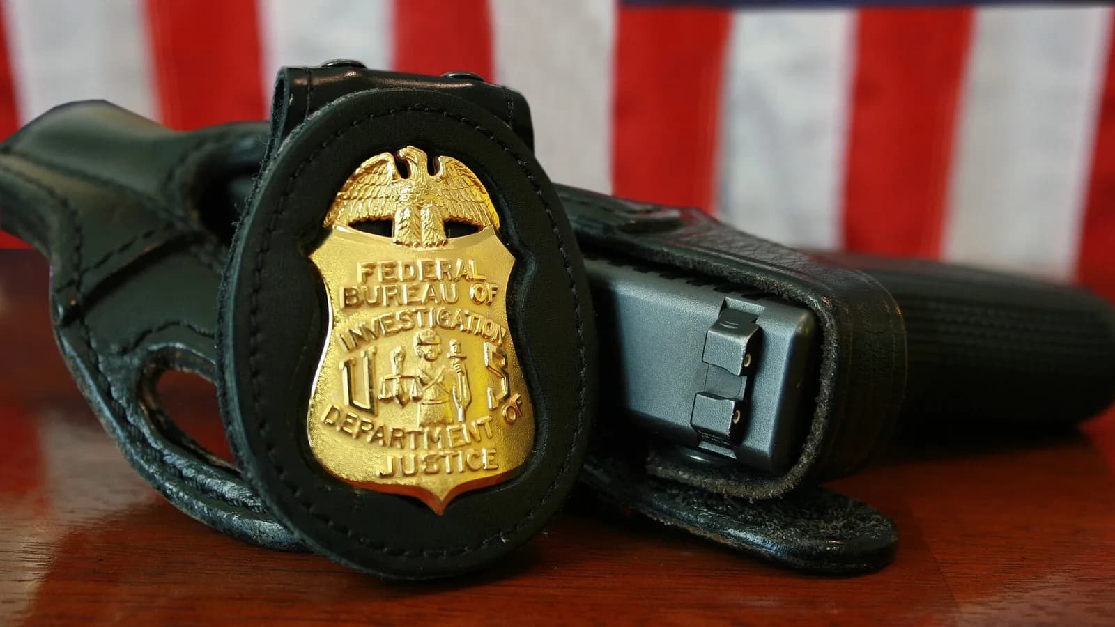 An FBI badge in a leather holder beside a holstered pistol on a wooden desk in front of an American flag, an undated file photograph illustrative of the FBI agents in the series and not a still from it