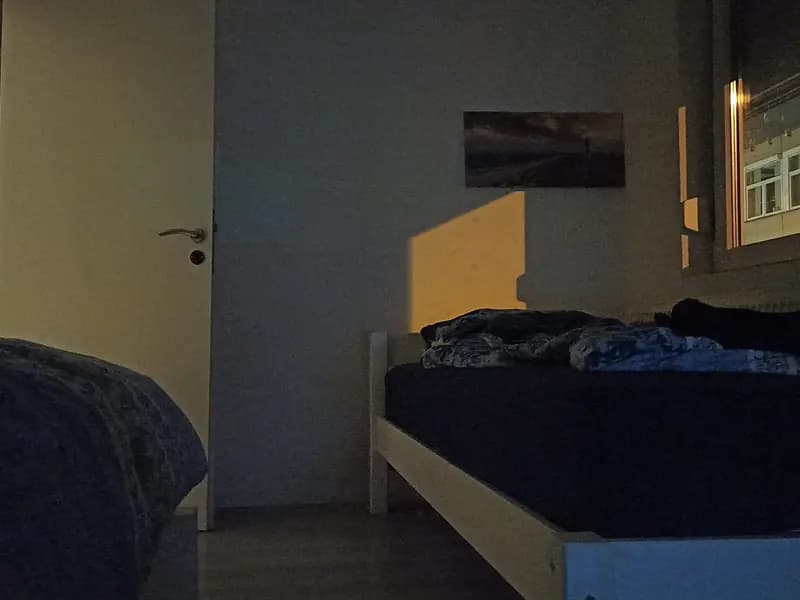 A dark bedroom at night with a street light shining through the window onto the bed, the kind of low light the study measured