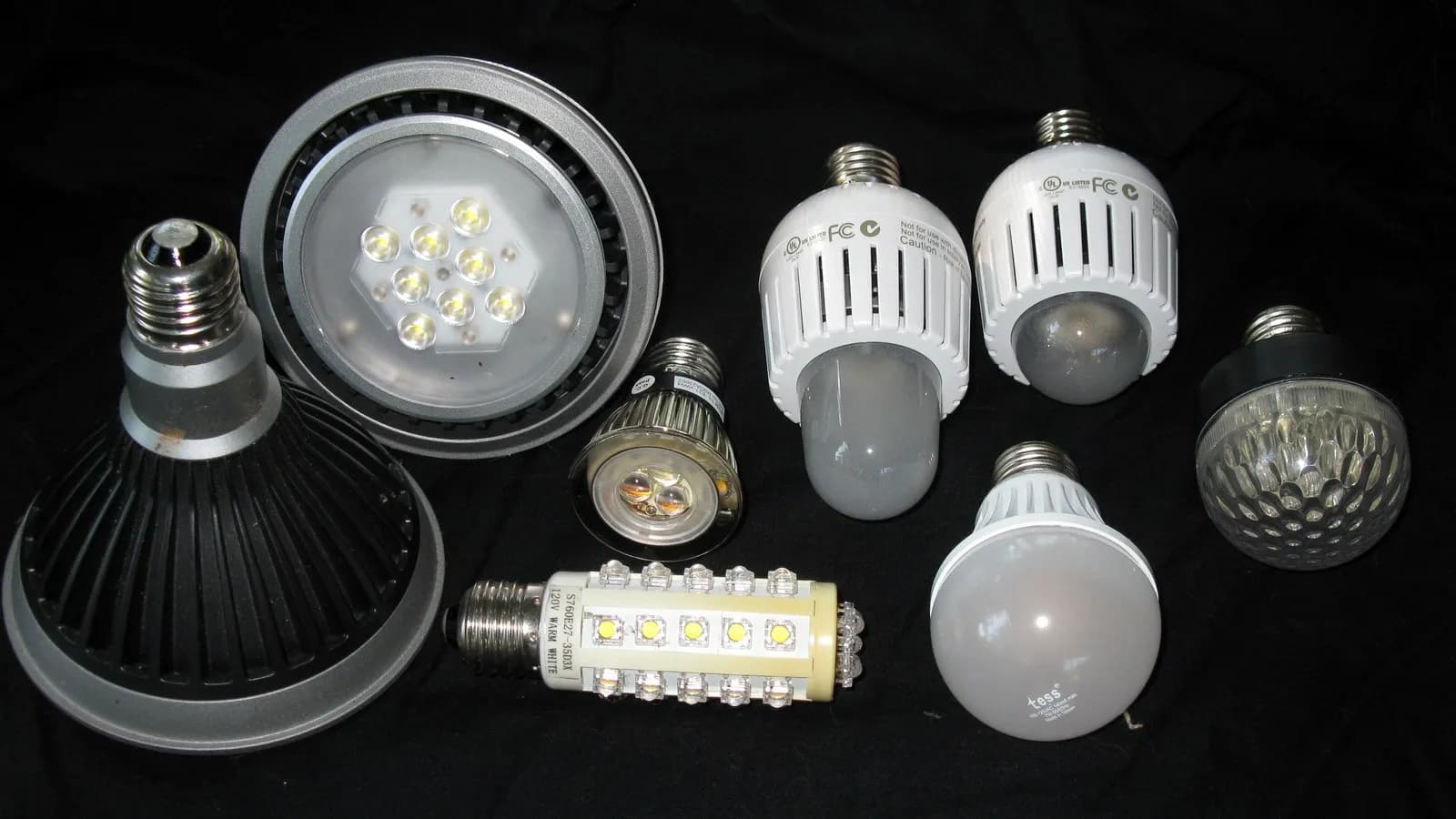 A selection of LED light bulbs of different shapes and sizes laid out on a dark cloth, photographed in July 2010