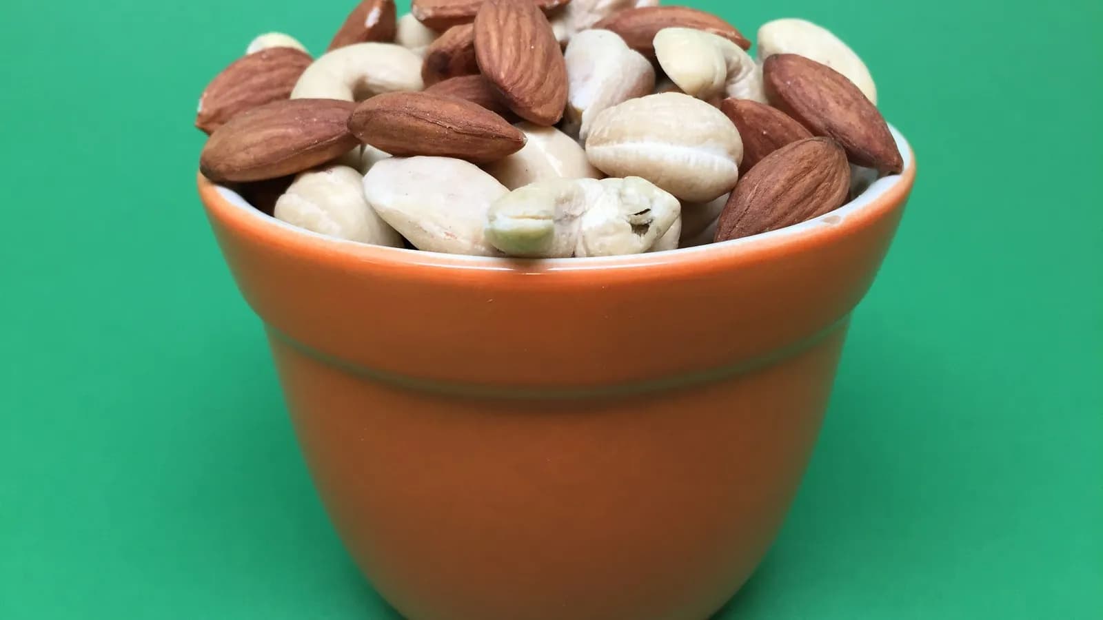 A small terracotta pot filled with almonds and cashews against a green background, two of the nut sources of magnesium, photographed in June 2018