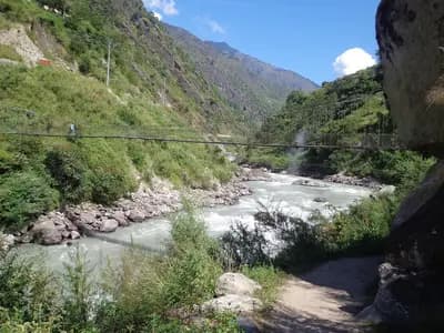The Trishuli river running fast through a steep, narrow Himalayan valley in Nepal, with a footbridge crossing it