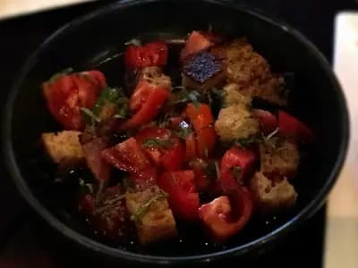 A dark bowl of panzanella, chunks of ripe tomato and toasted bread tossed with herbs and dressed in oil