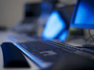 Computers on a long office desk, photographed out of focus. The keys used in the exploit were traced to a developer machine holding backups for seven of them