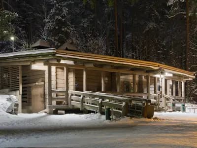 The public smoke sauna at Kuusijärvi in Vantaa, Finland, its timber walls lit at night with snow on the ground and the forest behind