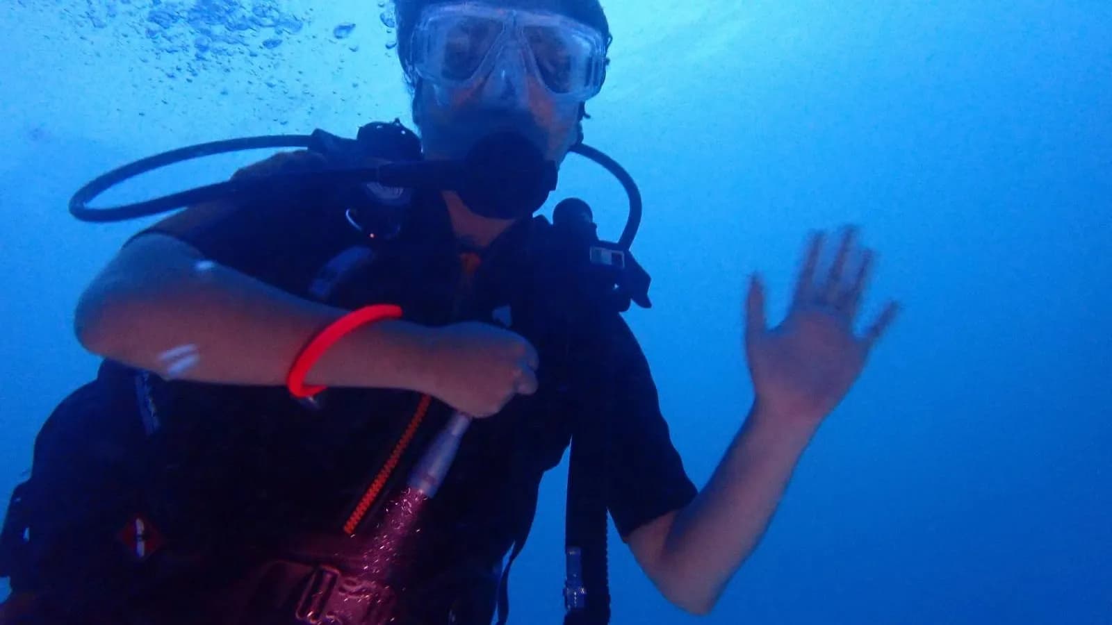 A scuba diver underwater in blue water, hand raised toward the camera, in a 2024 photograph