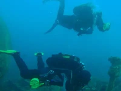 A scuba diver preparing to deploy a delayed surface marker buoy at depth, beside the boiler of a wreck