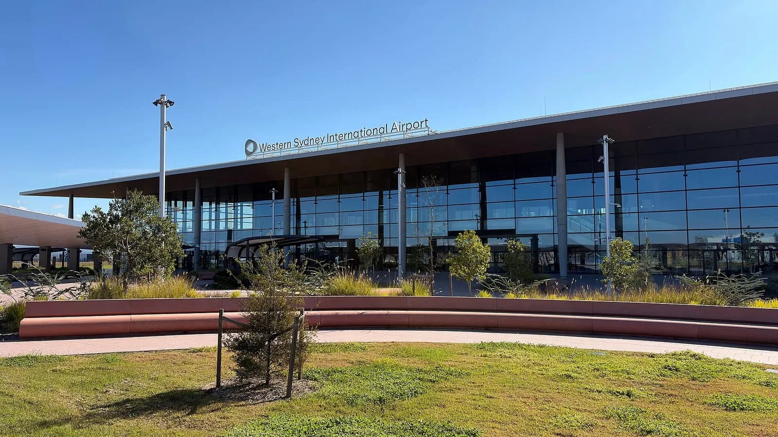 The glass-fronted terminal building of Western Sydney International Airport under a blue sky, with its name above the entrance, photographed in July 2026, a file photograph of the terminal before the first passenger flights